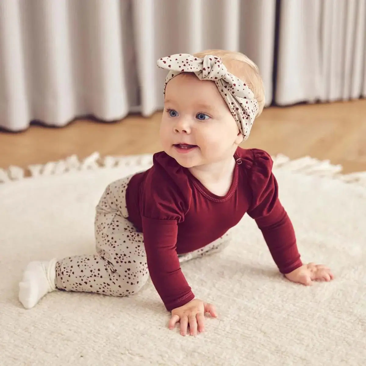 Baby wearing a maroon puff sleeve bodysuit and polka dot leggings, crawling on a soft carpet, showcasing Langarmbody &quot;Puff&quot; style.