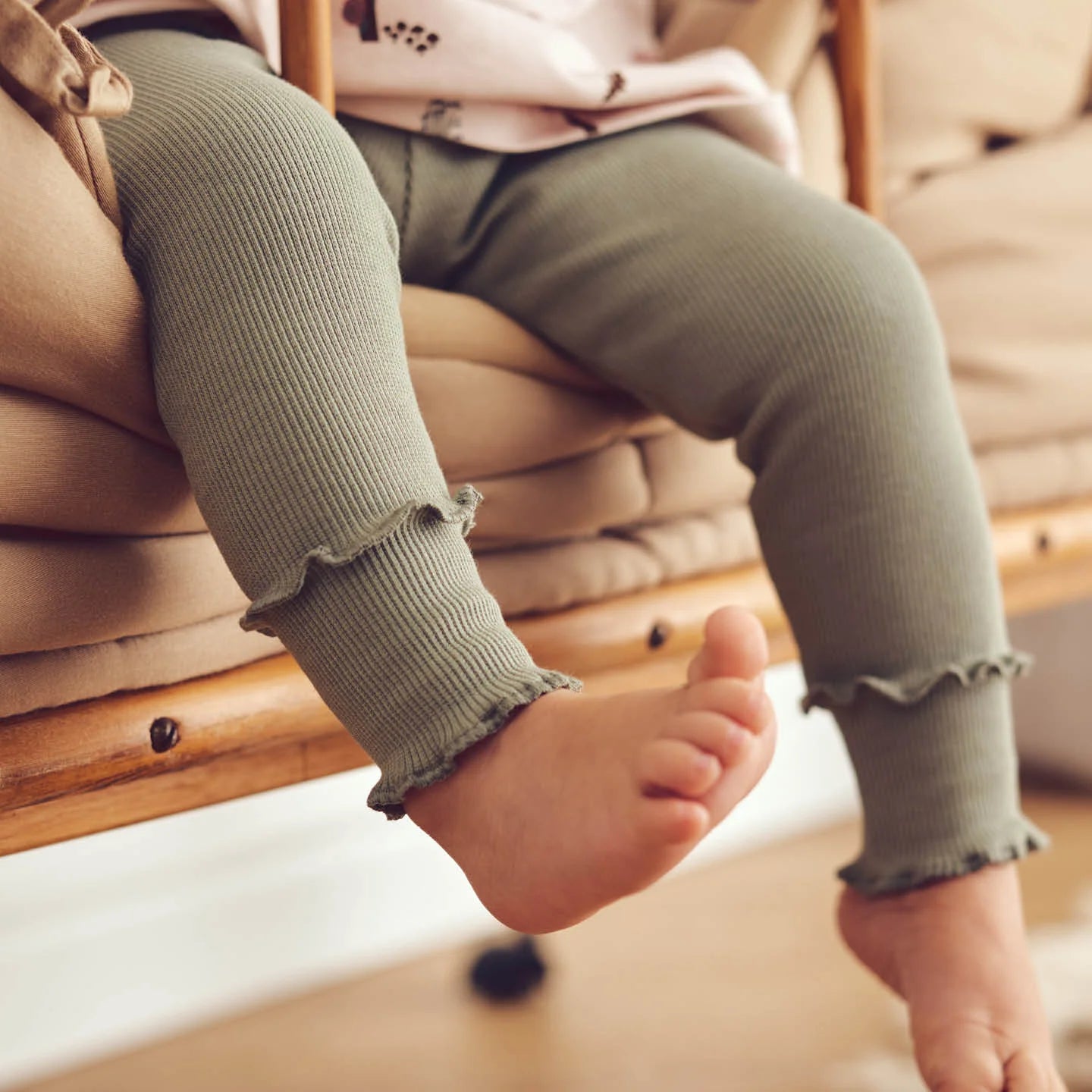 Baby wearing green Pointelle-quality leggings with ruffled edges, sitting comfortably on a chair.