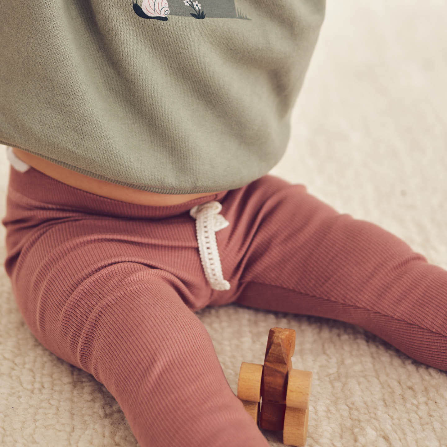 Baby wearing Pointelle leggings playing on soft carpet with wooden blocks.