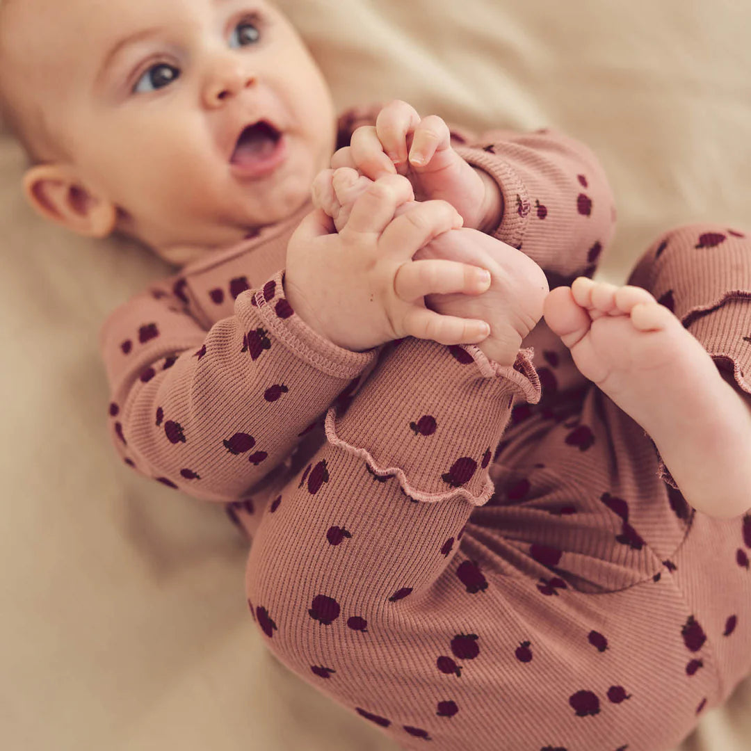 Baby wearing apple-patterned pointelle leggings with excellent fit and comfort, lying on a beige blanket.