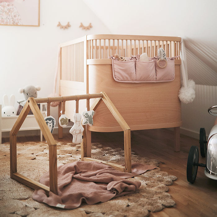 Wooden baby gym in nursery with crib, plush toys, and a cozy blanket on the floor, complementing the neutral decor.