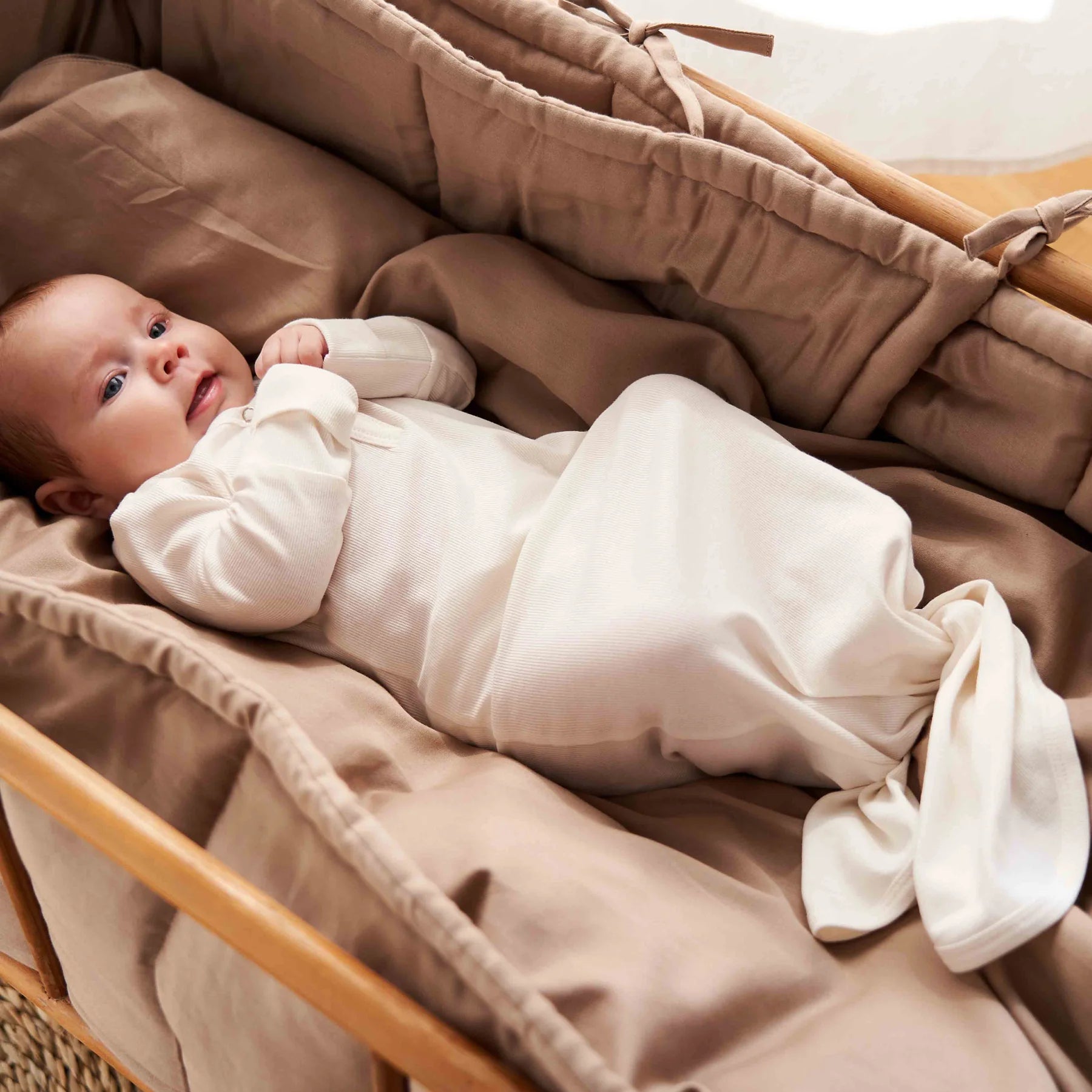 Baby in a soft knotted sleep gown with ribbed pattern, ideal for easy diaper changes, in a cozy and padded crib.