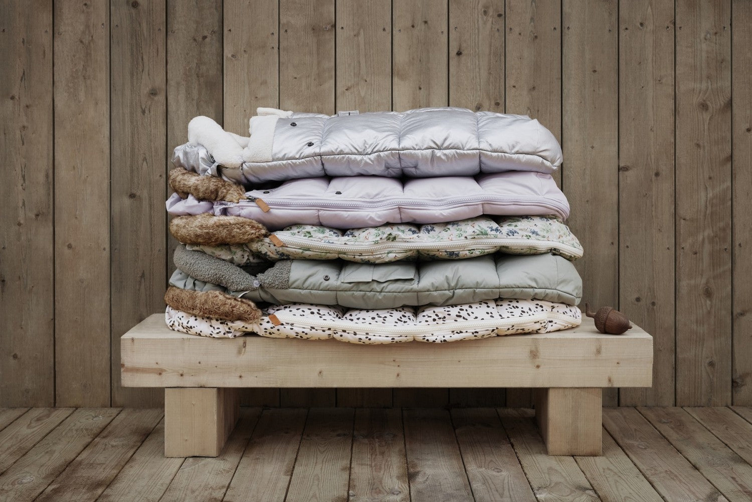 Stack of cozy footmuffs with modern design and thick padding, ideal for cold winter days, on a wooden bench.