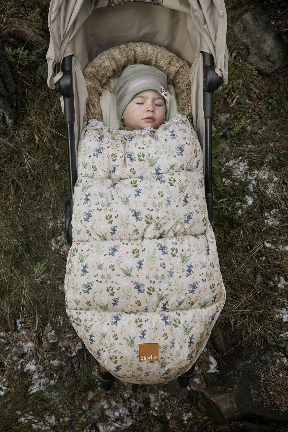 Baby cozy in Fairytale Forest Fußsack, floral design, in stroller outdoors on winter day.