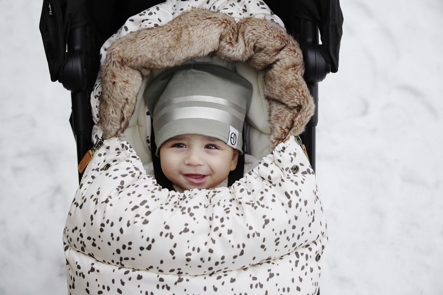 Baby smiling in stroller with Dalmatian Dots Fußsack, ideal for winter warmth and style.