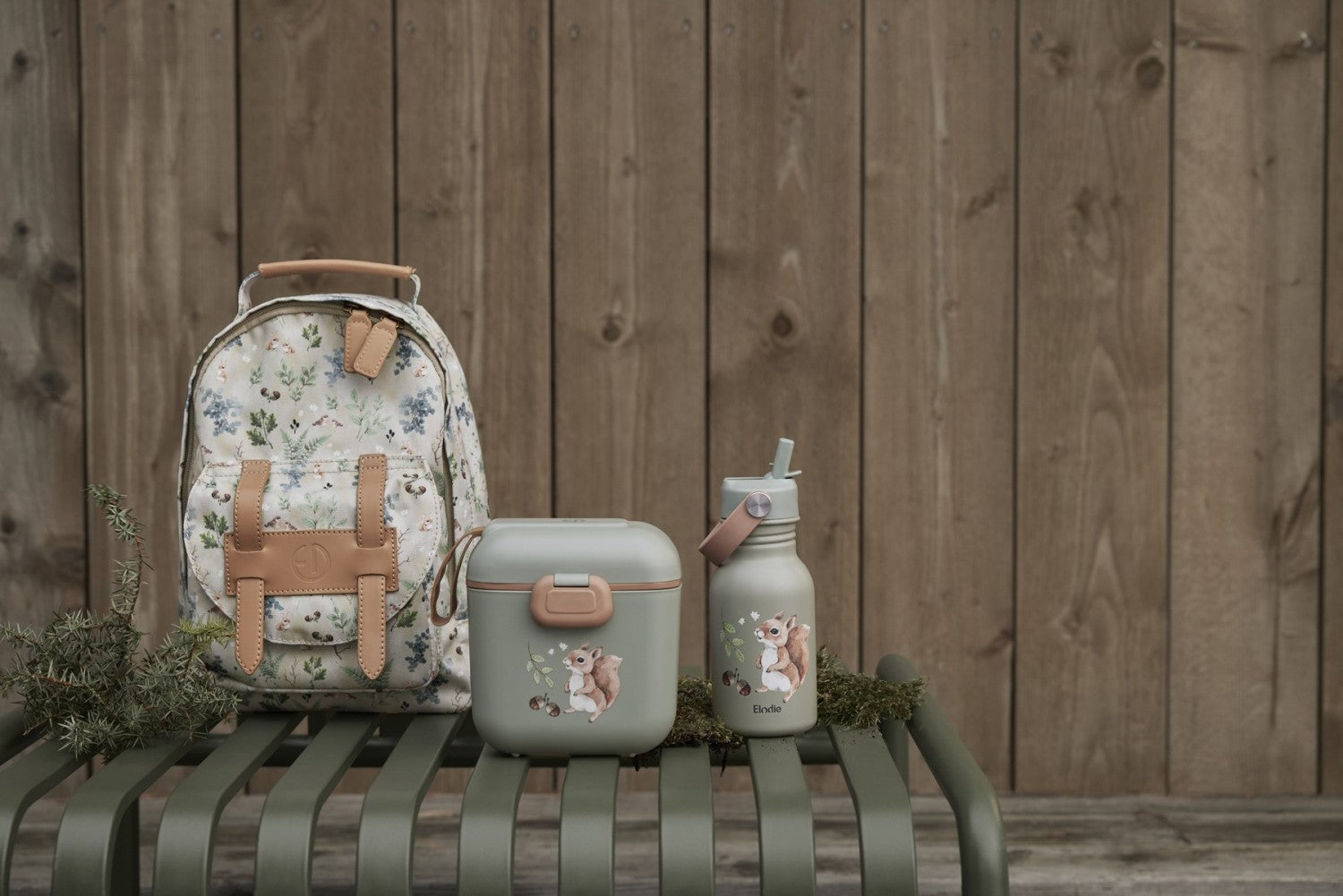 Kinderrucksack Fairytale Forest with matching lunch box and bottle on a green bench against a wooden fence background.