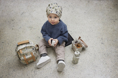 Toddler with fairytale forest backpack and lunch accessories sitting on the floor.