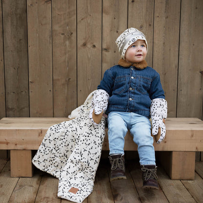 Toddler wearing Dalmatian Dots Fäustlinge and matching accessories, sitting on a wooden bench.